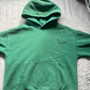 Grön hoodie från Zara - Säljer en grön hoodie från Zara med magficka och huva. Tröjan har en liten svart textdetalj på bröstet och är perfekt för en avslappnad stil. Passar dig som gillar bekväma och stilrena plagg.