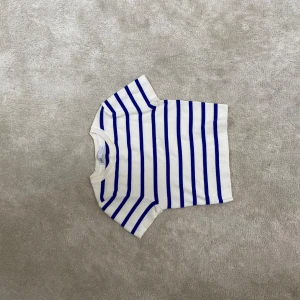 Vit och blå randig stickad topp - Vit stickad topp med blåa horisontella ränder. Kortärmad och med rund halsringning. Storlek M men sitter bra på mig som har xs