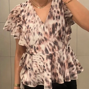 Söt Leopardmönstrad blus med volanger - Säljer en snygg leopardmönstrad omlottblus från Lipsy med volangärmar och knyt i midjan. Blusen har v-ringning. Storlek M/38, men passar mig som vanligtvis har storlek S. På bilderna där jag bär den har jag satt en säkerhetsnål vid V-ringningen. 
