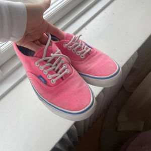 Rosa Vans sneakers med vita snören - Säljer ett par klassiska Vans sneakers i en snygg rosa färg med vita snören och vit sula med blå rand. Skorna har låg modell och rund tå, perfekta för dig som gillar färg och streetstil. Skorna ska föreställa 39 men känns mer som 38!