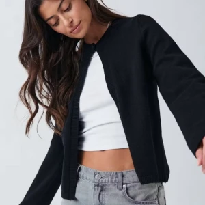 Svart kofta med rund hals - En enkel och stilren svart kofta med rund hals och långa ärmar. Koftan har en knapp upptill och är tillverkad i ett mjukt stickat material. Perfekt att slänga över en topp för en avslappnad look.