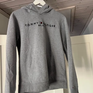 Tommy Hilfiger hoodie - Säljer denna Tommy Hilfiger hoodien då den blivit för liten för mig. Hoodien är i storlek 176 vilket motsvarar XS/S. Vill du ha en hoodie som inte sitter så baggy är denna perfekt! Hoodien har inga defekter. Vid minsta fundering är det bara att höra av sig!