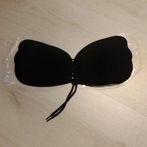 Svart självhäftande behå c kupa - Säljer en svart behå med snörning framtill.Behån har en slät yta och är formad för att ge stöd utan axelband. Perfekt för outfits där du vill ha en osynlig look under kläderna.