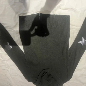 Mörkgrå stickad polotröja med stjärnor - Säljer en mörkgrå stickad polotröja med långa ärmar. Tröjan har silvriga stjärnor på ärmarna som snygg detalj. Perfekt för dig som vill ha något både bekvämt och trendigt.