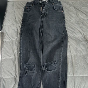 Svarta jeans med slitna knän från g perfect jeans - Säljer ett par svarta jeans från g perfect jeans med raka ben och slitna detaljer vid båda knäna. Jeansen har klassisk femficksdesign och dragkedja. Perfekta för en avslappnad och trendig stil.