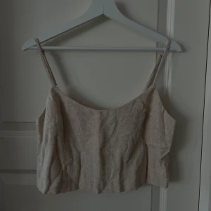Beige  croppad linne - Säljer en stilren beige linnetopp med smala axelband. Toppen är croppad och har en enkel, rak passform. Perfekt för varma dagar och enkel att matcha med olika outfits. Kollektion Lisa&Lena för NA-KD
