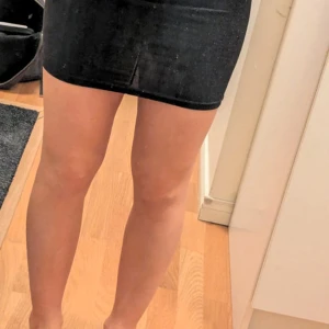 Svart glittrig minikjol - Säljer en svart glittrig minikjol med tight passform. Kjolen är kort och har en diskret slits framtill. Perfekt för dig som vill ha en enkel men ändå festlig look. Materialet är stretchigt och bekvämt.