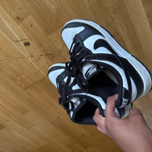 Nike Dunk Low svartvita sneakers - Säljer ett par klassiska Nike Dunk Low sneakers i svart och vitt. Skorna har svart snörning, vit tåbox och sidor samt svarta detaljer och Nike-logga på sidan. Perfekta för dig som gillar streetwear och vill ha en tidlös look.