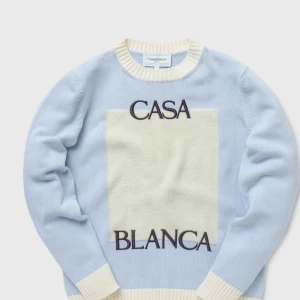 Ljusblå stickad tröja från Casablanca - Säljer en ljusblå stickad tröja från Casablanca med krämvita ribbade muddar och en stor krämvit ruta framtill. Svart text 'CASA BLANCA' på bröstet. Perfekt för dig som gillar stilrena och unika plagg. Passar S 