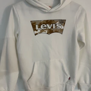 Levi's hoodie  - Säljer en vit hoodie från Levi's med en kamouflagemönstrad logga på bröstet. 