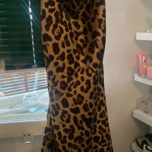 Leopardmönstrad långklänning i satin - Säljer en snygg långklänning med leopardmönster i bruna och svarta toner. Klänningen har en slät satinfinish som ger ett lyxigt intryck och ett elegant fall. Perfekt för dig som vill sticka ut med en trendig look.