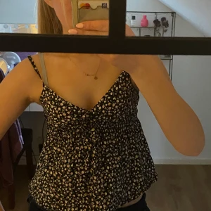 Blommig linne från Design by si - Säljer ett sött blommigt linne från Design by si. Det är svart med små vita  blommor med gröna små blad. Linnet har smala reglerbara axelband och en luftig passform med smock (det skrynkliga/stretchiga) under bysten och i ryggen för en perfekt passform, perfekt för varma dagar. Han används några gånger utan tecken på defekter. Hör av dig vid frågor💞