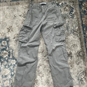 Grå cargobyxor med fickor - Säljer ett par snygga gråa cargos från bershka med jätte coola fickor bakom och på sidan, tyvärr har den ett par hål på slutet och lite smuts som går ej bort med våra medlar för tvättning, därför läggs priset