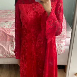 Röd sammetsklänning med spetsärmar från Lindex - Säljer en röd sammetsklänning från Lindex med långa spetsärmar och utsvängda ärmslut. Klänningen har en mjuk sammetskänsla och fina spetsdetaljer upptill och på ärmarna. Perfekt för dig som vill sticka ut med en färgstark look!