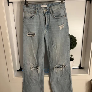 Ljusblå slitna jeans från Zara - Ljusblå jeans från Zara med raka ben och flera slitningar framtill. Klassisk femficksmodell med normal passform och hög midja. Perfekta för en avslappnad och trendig look.
