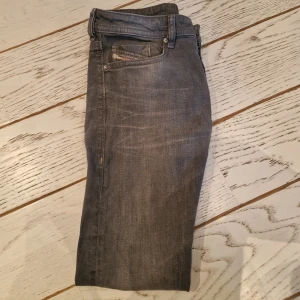 Grå jeansbyxor från Diesel - Säljer ett par grå jeansbyxor från Diesel med klassisk femficksdesign och knappar i gylfen. Byxorna har raka ben och diskreta slitningar för en snygg, använd look. Perfekta för dig som gillar stilrena och tidlösa jeans.