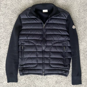 Mörkblå Moncler cardigan - Snygg mörkblå cardigan jacka från Moncler med dragkedja framtill och två fickor med dragkedja. Jackan har långärmade stickade ärmar och Moncler-logga på ena ärmen. Perfekt för kyliga dagar.