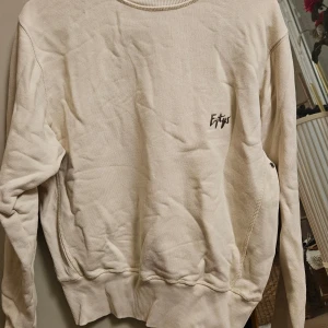 Beige sweatshirt från Eytys - Säljer en beige sweatshirt från Eytys med rund halsringning och diskret logga på bröstet. Tröjan har långa ärmar och ribbade muddar vid ärmslut och nederkant. Perfekt för en avslappnad stil. Storlek för kvinna är XS och för man är XXS.