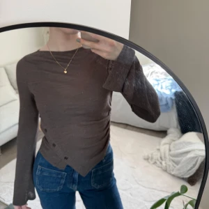 Brun långärmad topp från NA-KD - Säljer en brun långärmad topp från NA-KD med lätt utsvängda ärmslut och asymmetrisk nederkant. Tunn och mjuk i materialet, perfekt till jeans eller kjol. Enkel och stilren design.