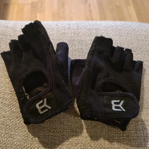 Svarta fingerlösa handskar, styrketräningshandskar - Säljer ett par svarta fingerlösa handskar med vaddering i handflatan och justerbar rem vid handleden. Perfekta för aktiviteter som kräver bra grepp och rörelsefrihet. De har en stilren design med en logotyp på ovansidan. Märke: better bodies. Storlek: S. Använt skick! Noppig dock finns funktionen kvar. 