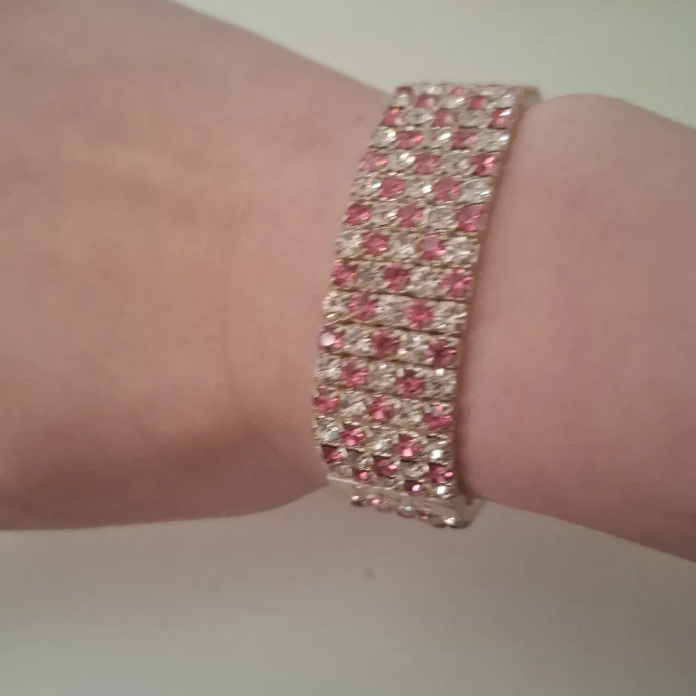 Snyggt glittrigt armband från SNÖ med rosa och klara stenar. Armbandet har en bred design och är perfekt för att ge en extra touch till din outfit. Det elastiska bandet gör det enkelt att ta på och av.. Asusteet.