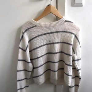 Vit och grå randig stickad tröja - Säljer en mysig vit stickad tröja med gråa ränder. Tröjan har en rund hals och långa ärmar, perfekt för kyligare dagar. Den är både stilren och bekväm, ett måste i garderoben!