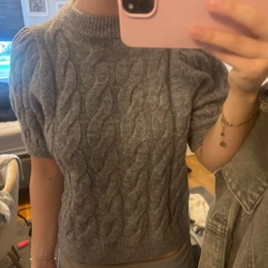 Grå stickad topp från Gina Tricot - Säljer en grå stickad topp från Gina Tricot med kabelstickat mönster. Toppen har korta ärmar och en rund halsringning. Aldrig använt. 