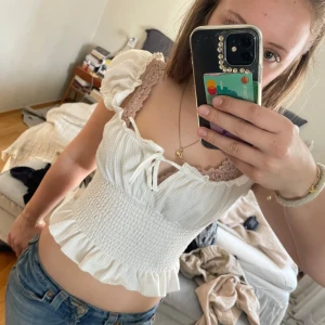 Vit topp från Gina Tricot - ‼️INTRESSEKOLL! Skriv innan ni köper‼️Säljer en söt vit topp från Gina Tricot med volangdetaljer och knytning framtill. Toppen har korta ärmar och en smockad design som ger en fin passform. Perfekt för sommarens alla tillfällen! 🌸