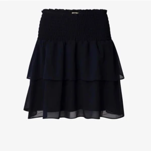 Svart volangkjol från Chelsea - Snygg svart kortkjol från Chelsea med volanger och elastisk midja. Perfekt nu till sommaren!Kjolen har en luftig design som ger en fin rörelse.