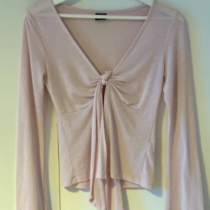 Ljusrosa långärmad topp med knyt från Gina Tricot - Supersöt ljusrosa långärmad topp från Gina Tricot med v-ringning och knyt framtill. Tunn och mjuk i materialet, perfekt för lager-på-lager eller som den är. Enkel att styla till olika outfits.