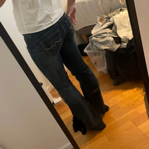 Mörkblå bootcut jeansbyxor med fickdetaljer - Säljer ett par super snygga  mörkblå jeansbyxor med bootcut passform från pepe jeans! Byxorna har dekorativa fickor både fram och bak samt kontrastsömmar. Klassisk jeanslook med låg midja och utsvängda ben. Mått: midjemått 34, Innerbenslängd 75