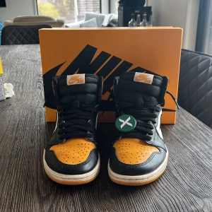 Nike Air Jordan 1 Retro High OG 'Taxi’  - Säljer ett par Nike Air Jordan 1 Retro High OG 'Yellow Toe' med svart, gul och vit färgkombination. Skorna har klassisk hög siluett, svart snörning och rund tå. Perfekta för dig som vill sticka ut med en ikonisk sneaker. Nypris går för ca 1500 kr och jag säljer för 749 kr