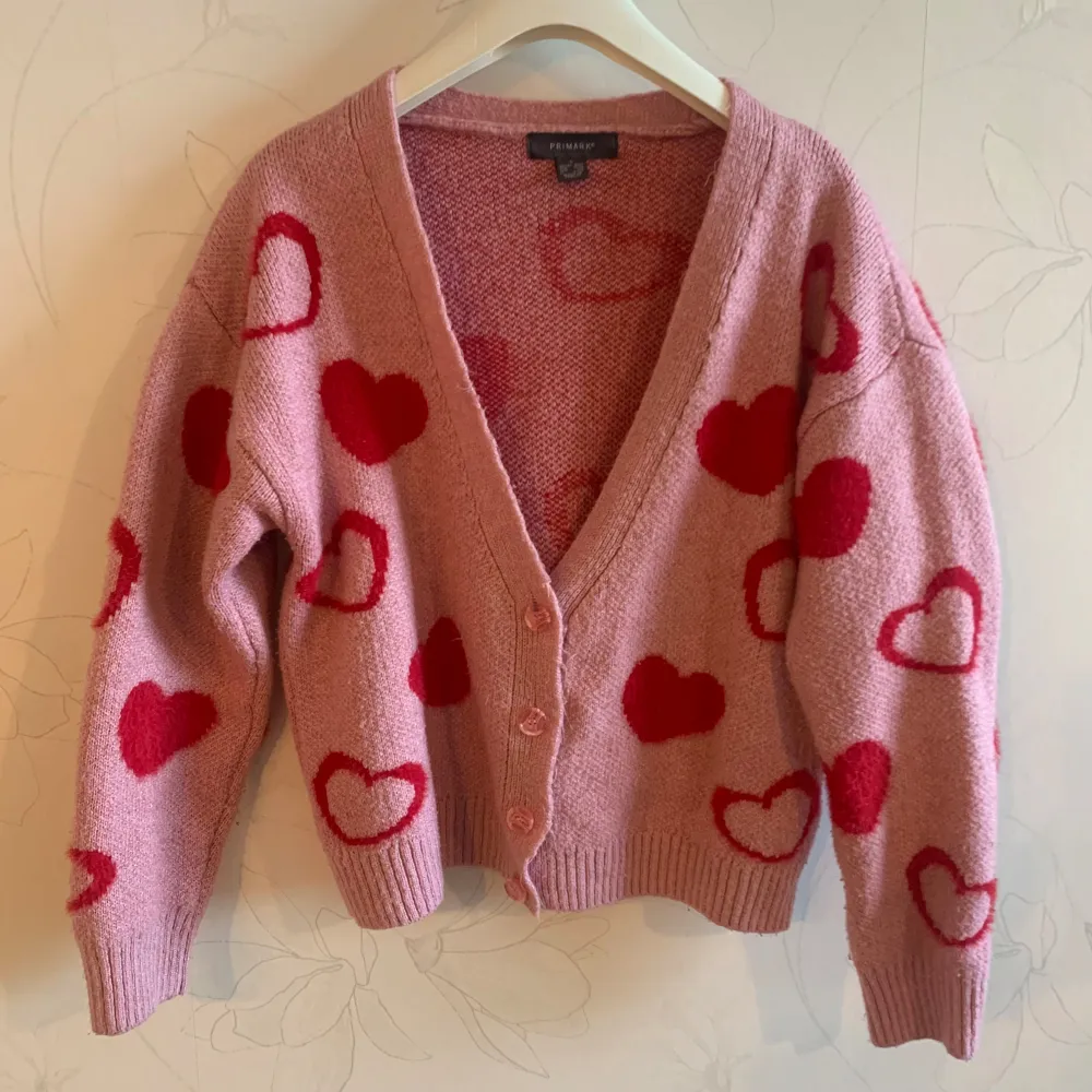 Säljer en söt rosa kofta från Primark med röda hjärtan över hela. Koftan har en v-ringning och knappar framtill. Perfekt för att ge en fin touch till din outfit. 💖Kontakta mig gärna om du vill ha fler bilder eller om du har några funderingar! Priset går såklart att diskutera!. Neuletakit & Villapaidat.