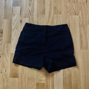 Svarta shorts med normal passform - Svarta shorts med klassisk design och normal passform. De har bälteshällor och stängs med dragkedja och knapp framtill. Perfekta för varma dagar och enkla att matcha med olika toppar.