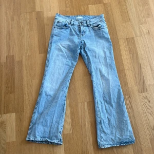 Ljusblå bootcut jeans - Säljer ett par ljusblå bootcut jeans med klassisk femficksdesign och lågmidja. Jeansen har en bekväm passform och är perfekta för en avslappnad stil. De har en dragkedja och knapp framtill.