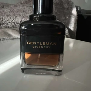 Gentleman Givenchy Parfym - Elegant herrparfym från Givenchy i en stilren flaska med svart och transparent design. Doften är maskulin och sofistikerad, perfekt för den moderna gentlemannen. Flaskan har en praktisk sprayfunktion.
