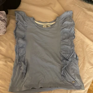 Ljusblå topp från Hampton Republic - Säljer en söt ljusblå topp från Hampton Republic med volangdetaljer längs sidorna. Perfekt för en somrig look. Toppen är ärmlös och har en rund halsringning.