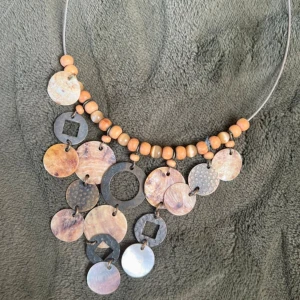 Halsband med träpärlor och metallbrickor - Unikt halsband med en mix av träpärlor och metallbrickor i olika former och färger. Designen har en bohemisk känsla med runda och fyrkantiga detaljer som hänger i olika nivåer. Perfekt för att ge en naturlig touch till din stil.