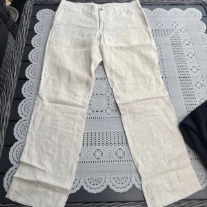 Beige linnebyxor 31/32 - Snygga beige linnebyxor med hög midja och raka ben. Perfekta för en avslappnad och stilren look. Byxorna har en enkel design med knappar framtill.