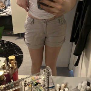 Beige shorts från Gina Tricot - Säljer ett par beige shorts från Gina Tricot med normal passform. Shortsen har fickor både fram och bak samt knäppning med dragkedja och knapp. Perfekta för varma dagar och enkla att matcha med olika toppar.