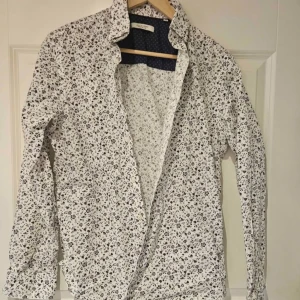 Vit blommig skjorta från Jack & Jones Premium - Säljer en vit skjorta från Jack & Jones Premium med små blommiga mönster i svart och beige. Skjortan har lång ärm och klassisk krage, perfekt för dig som gillar stilrena men ändå unika plagg.