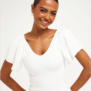 Vit gullig klänning - Säljer en stilren vit ribbad klänning med korta puffärmar och v-ringning från ONLY. Klänningen har en knytning i ryggen som ger en söt detalj. Perfekt för somriga dagar eller studenten🤍