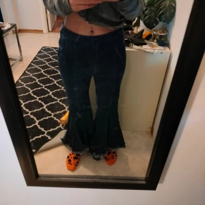 Mörkblå utsvängda jeans med råa kanter - Säljer ett par mörkblå jeans med extremt utsvängda ben och råa, fransiga kanter nertill. Byxorna är lågmidjade och har en unik, bohemisk look. Perfekta för dig som vill sticka ut med din stil.