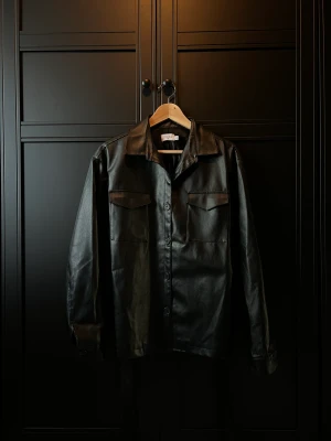 Svart skinnjacka med bälte från NA-KD  - Storlek: 40 Material: polyuretan/polyester  Skick: Inga anmärkningar 