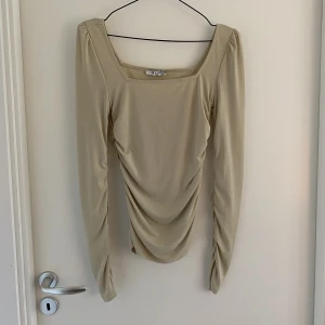 Topp med fyrakantigringning  - Har fyrkantig ringning och har rysch i sidorna och i ärmarna 