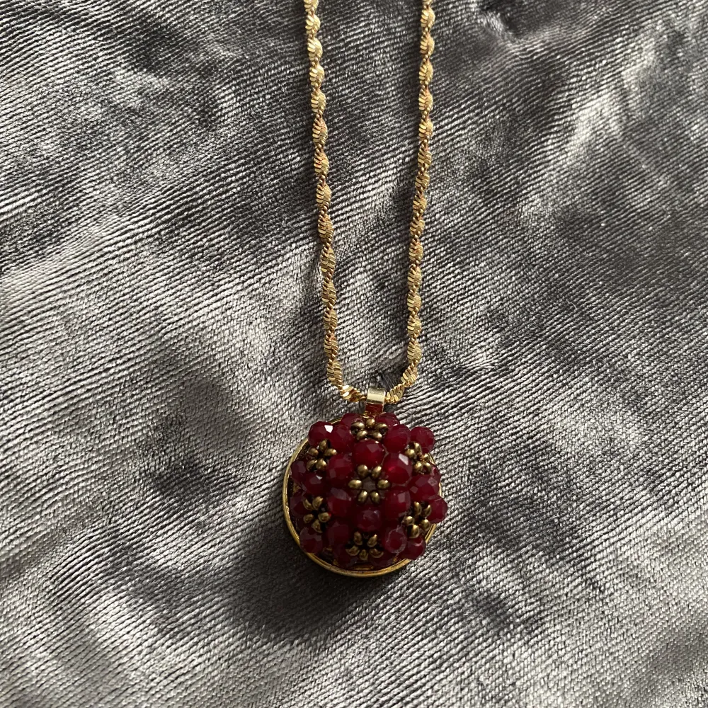 Ett fint guld halsband med en vinröd blomma. Accessoarer.