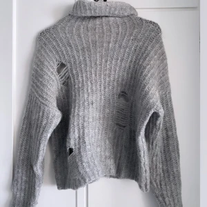 Grå stickad  - Grå stickad tröja med krage dessutom små hål runt tröjan som design!!