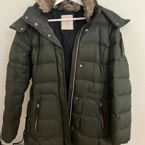 Esprit dunjacka  - Esprit dunjacka. Mörkgrön. Längre modell. Fuskpäls vid krage och luva. Varm/skön. Använd 1-2 ggr/köpte för stor stlk. 