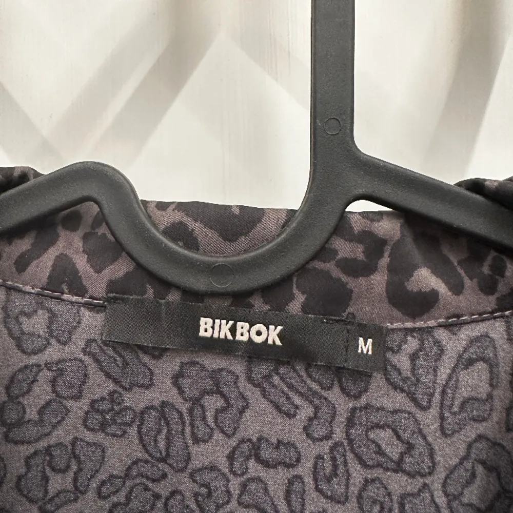 Grå blus från BikBok med svart leopardmönster. Saknas en knapp på en av armarna men är två knappar på varje arm så det syns inte tydligt. Har katt i hemmet men ej där kläderna är.. Blusar.