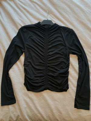 Svart tröja krinklade partier - Aldrig använd. Stretchigt material. Krinklad fram och bak samt i sidorna. Något liten i storleken passar M\L
